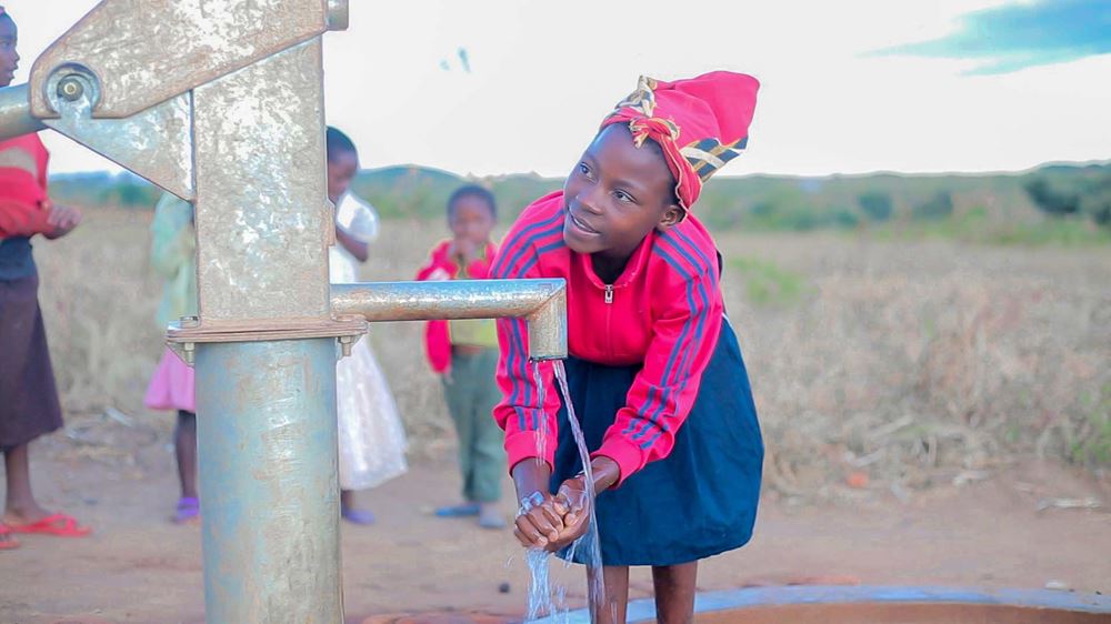 Mädchen wäscht sich die Hände am Brunnen 