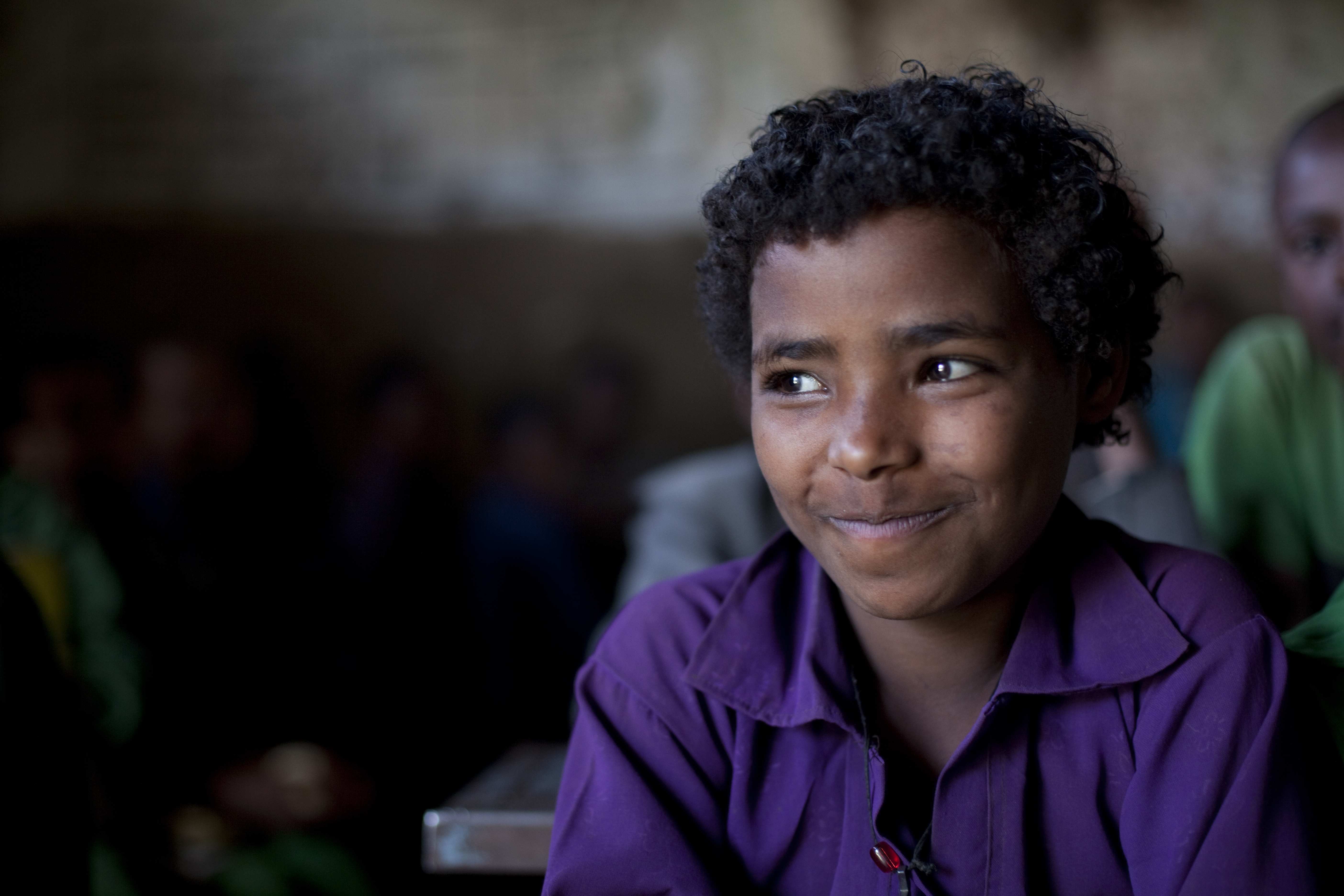 Lächelnder Junge aus Äthiopien - Humanitäre Hilfe für Dürreopfer in Äthiopien, Junge in lila Oberteil, schmunzelt, lächelt, Locken, sitzt, schaut zur Seite, Schule