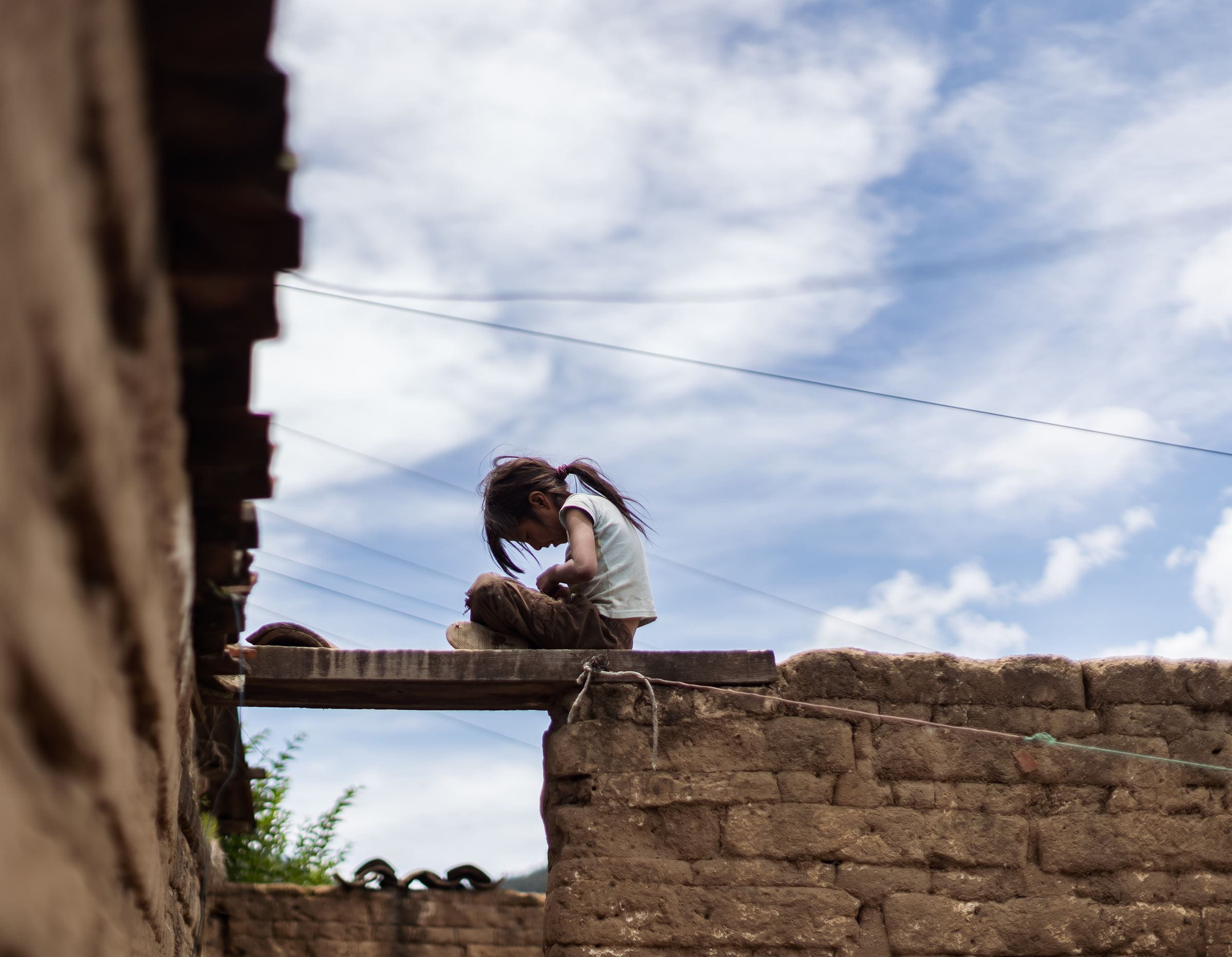 Ein Mädchen aus Guatemala sitzt in schmutziger Kleidung mit gebeugtem Kopf auf eine klapprigen Brücke. (Quelle: Jakob Studnar)